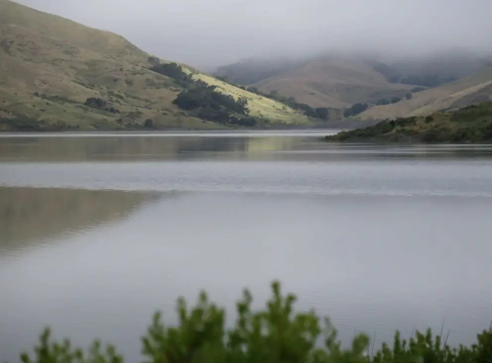 Mirrorlike water and sun hitting a distant hillside. 