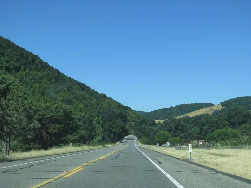Hill with leafy trees on one side, oak-studded yellow hill on the other, along Highway 46. 