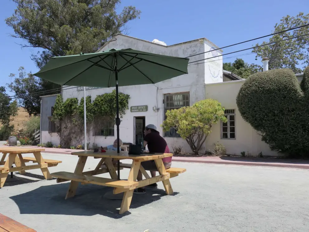 A dad and son eat at a picnic table, with the historic post office behind. 
