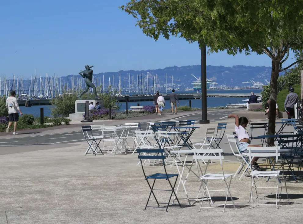 Tables and chairs by the William McCovey statue in China Basin Park, with South Beach Harbor across the water. 