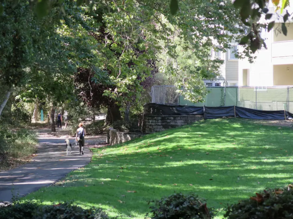 A lady walks her dog along the trail, past Avila Village. 