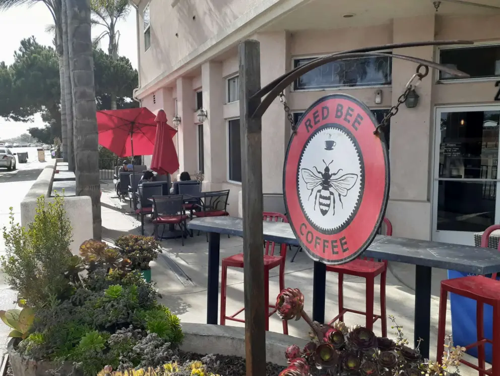 Seating under red umbrellas outside Red Bee Coffee. 