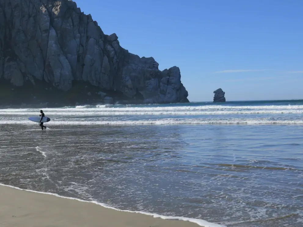 A surfer walks away, with stunning rock backdrop.