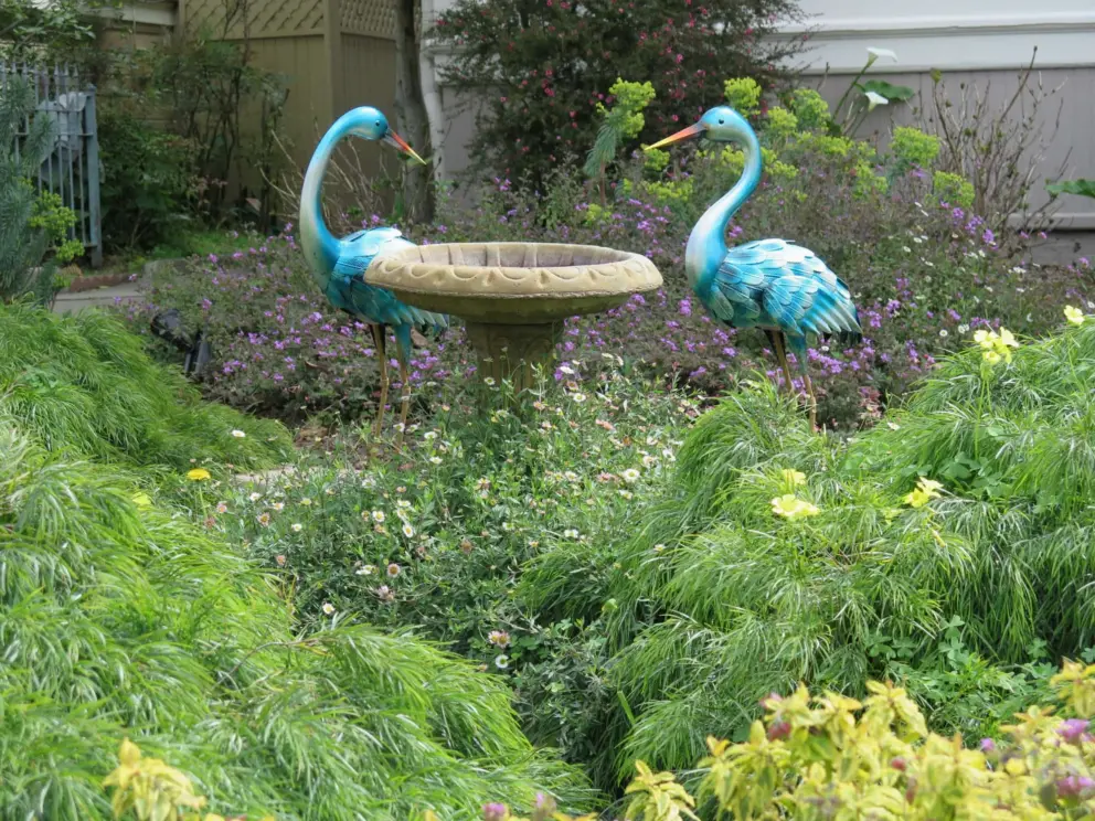 Bird statues around a bird bath, in a garden.