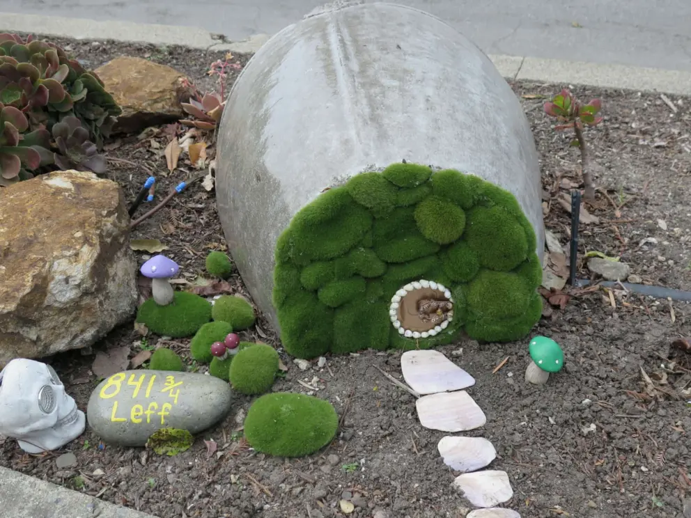 A hobbit house in a fairy garden, along the sidewalk. 