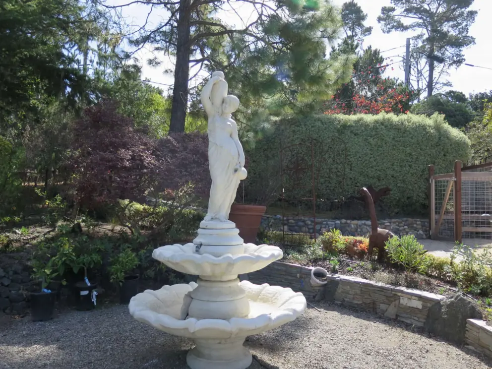 A young woman holding a pot fountain, where the path winds up an incline. 