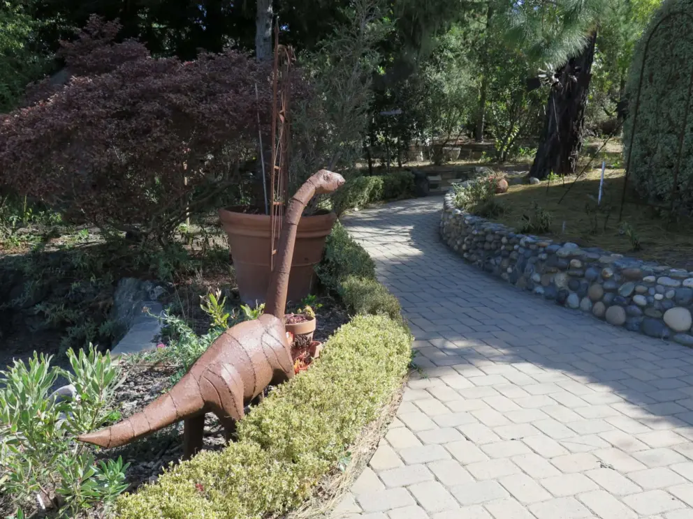 Metal dinosaur sculpture and stone wall, where the path winds around. 