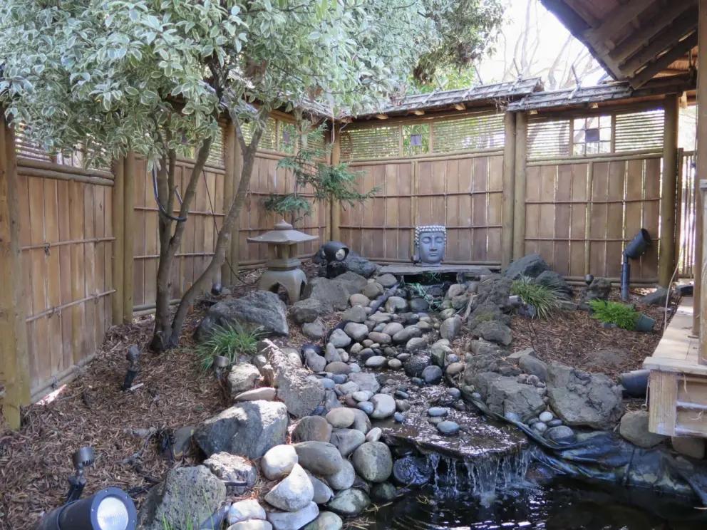 Buddha sculpture, spirit house, bamboo wall, and mini waterfall. 