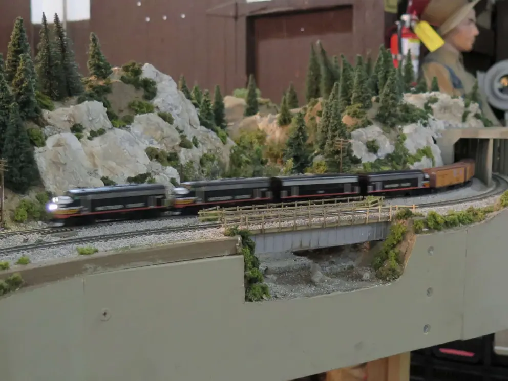 A model train heads through a tunnel in the mountains. 