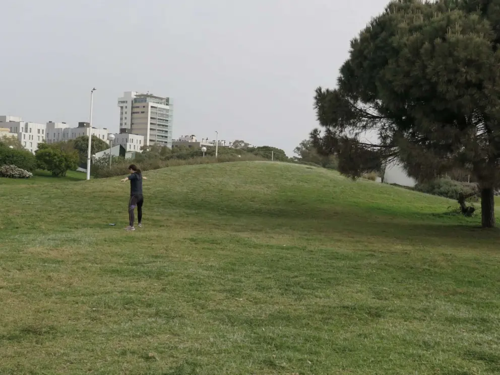 A lady does yoga on the lawn by a little hill.