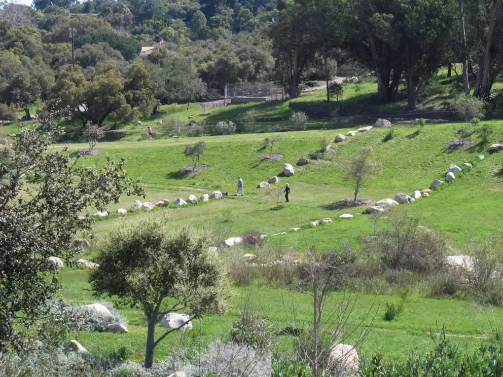 A couple walks on the grass between rows of boulders.