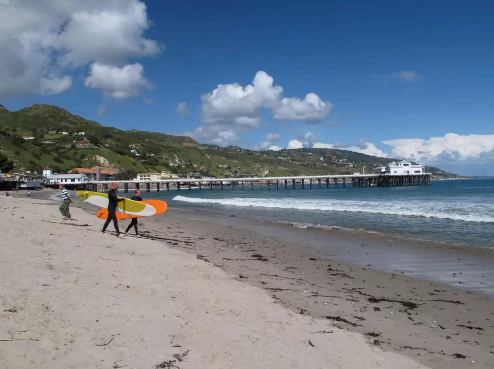 Longboarders walk down the beach.