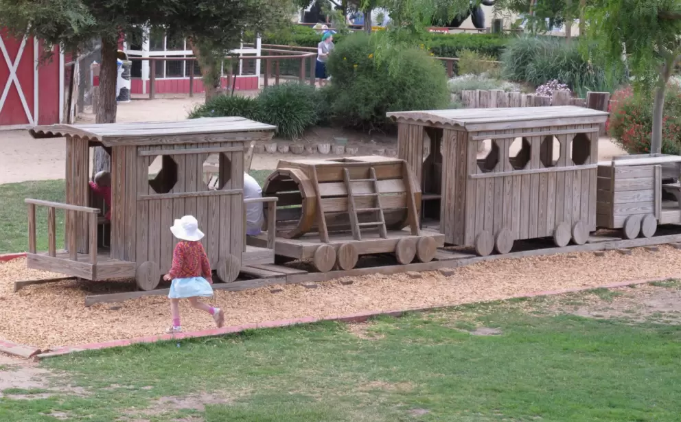 A little girl walks over to the long wooden train.