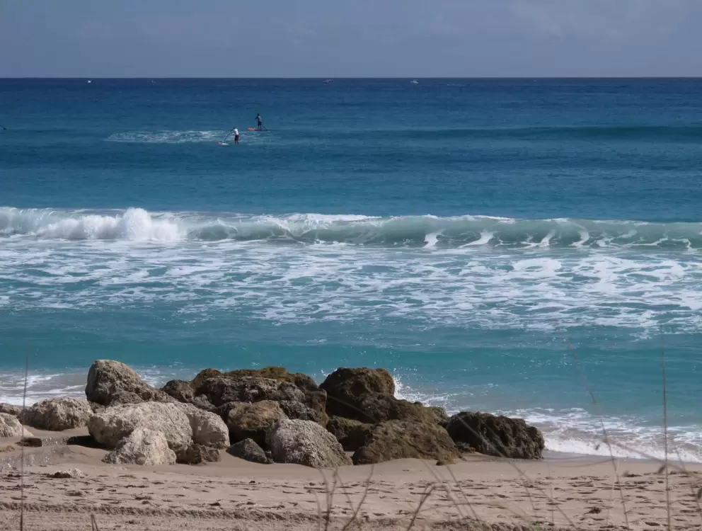 Rocks on the beach, and stand up paddle guys out in the water.