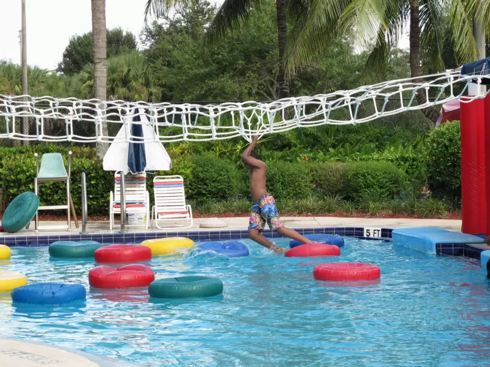 A boy tries his luck on the lily pad walk, a sort of monkey bar course above water!
