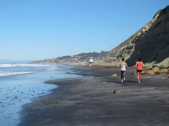 Beach with sparkling black sand, and hike atop high red cliffs with views.
