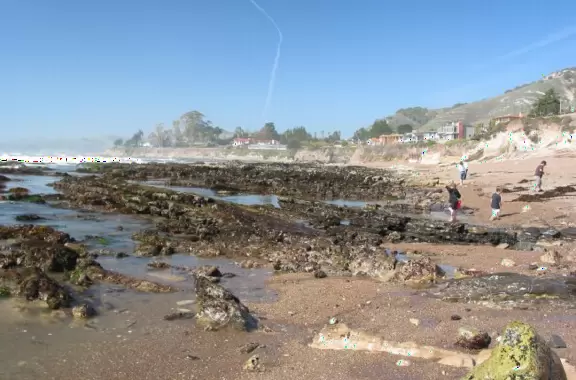 Walkway with benches above the ocean, and steps that lead down to tide pools and beach with reddish-hued sand and lovely cliffs.
