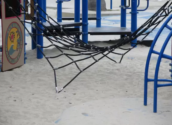 Playground by the sea with whale sculpture, shade canopies, climbies, spinning monkey bars, baby swings, low twisted trees to climb, and grass to run on.