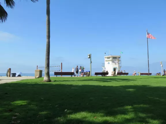 Fun beach with many spots to explore, including rock pools, a walking path with flowers above the sea, basketball courts, a playground, and a lawn by the beach.