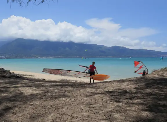 An incredibly beautiful beach with technicolor water, white sand strewn with coral, and colorful kite surfers zooming by, all framed by gorgeous mountains.