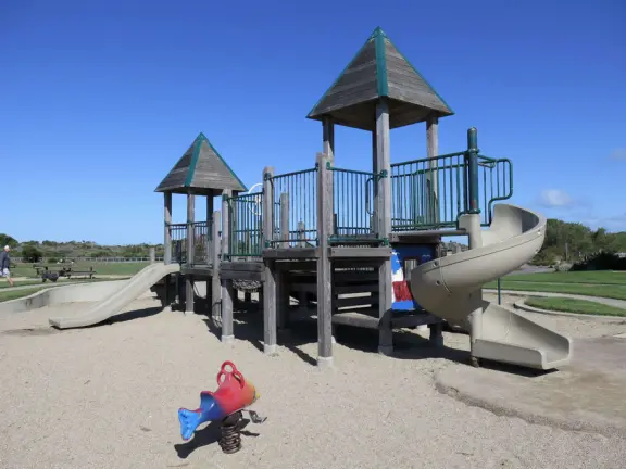 Wide open park behind the dunes in Morro Bay, with play structure with sand floor, and huge lawn with winding paths for tricycling.