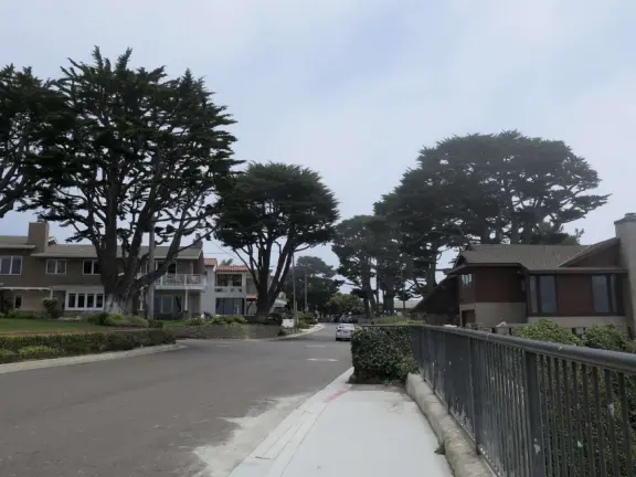 Walkway with benches above the ocean, and steps that lead down to tide pools and beach with reddish-hued sand and lovely cliffs.