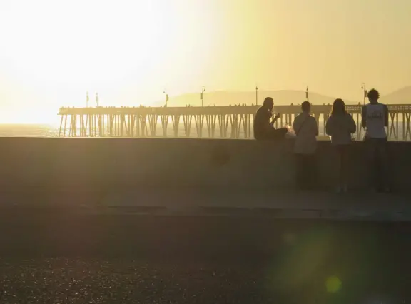 Gorgeous spot with wide pier, surfers carving the waves, whale playground, wide open attractive plaza, Pismo Beach selfie sign, and wooden promenade with views of the hills and sea.