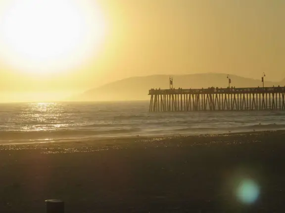 Gorgeous spot with wide pier, surfers carving the waves, whale playground, wide open attractive plaza, Pismo Beach selfie sign, and wooden promenade with views of the hills and sea.
