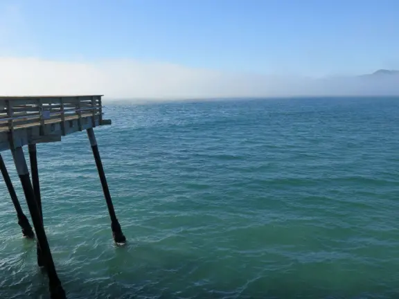 Gorgeous spot with wide pier, surfers carving the waves, whale playground, wide open attractive plaza, Pismo Beach selfie sign, and wooden promenade with views of the hills and sea.