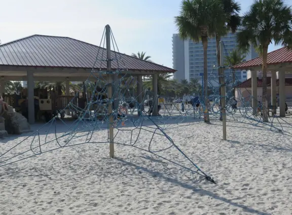 Two playgrounds (big and toddler) under huge shade canopies, on white sand, with two space nets, at the base of the gorgeous Pier 60.