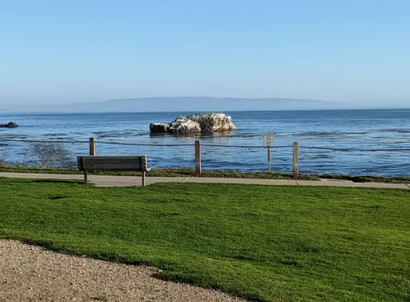 Walkway with benches above the ocean, and steps that lead down to tide pools and beach with reddish-hued sand and lovely cliffs.