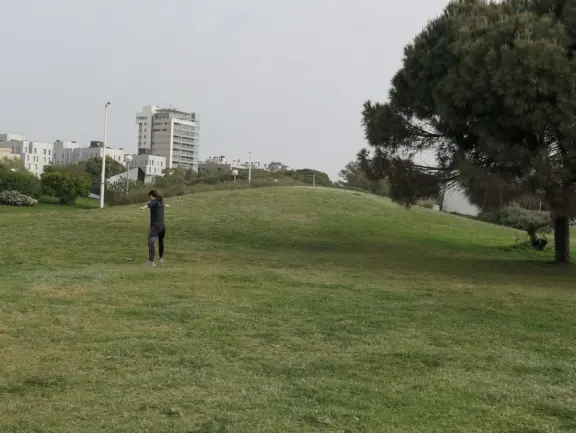 A lady does yoga on the lawn by a little hill.