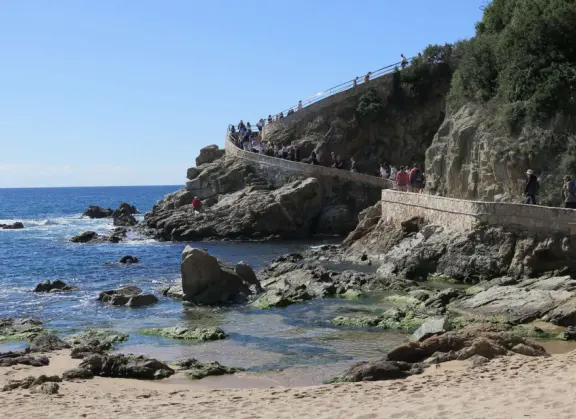 Clifftop up-and-down path with Dona Marinera statue, flowers, lovely cypress forest, and stunning views of the turquoise sea.